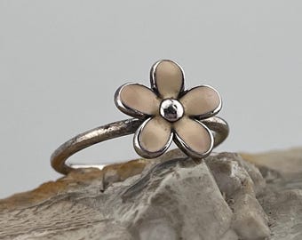 May include: A silver ring with a delicate, pale pink flower design. The flower has five petals and a small silver center.