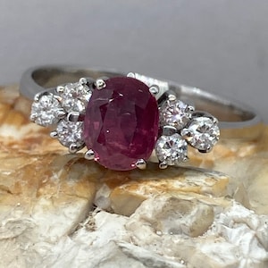 May include: A silver ring with a large oval-shaped ruby gemstone surrounded by smaller diamonds.