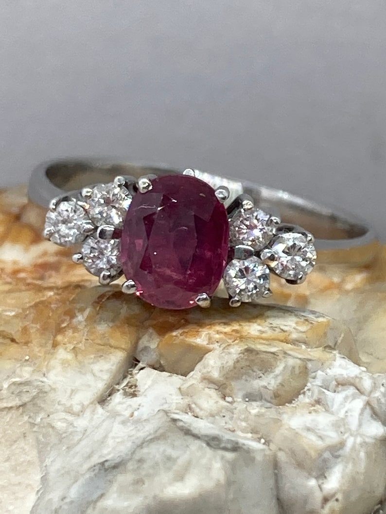 May include: A silver ring with a large oval-shaped ruby gemstone surrounded by smaller diamonds.