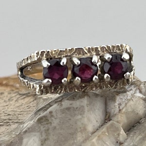 May include: A silver ring with three purple gemstones set in a textured band.