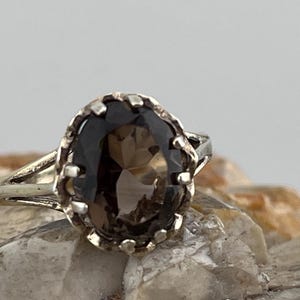 Peut inclure: Une bague en argent avec une grande pierre précieuse ovale de couleur brun foncé sertie dans une bélière décorative à festons.