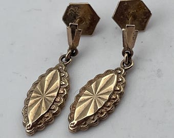 May include: A pair of gold drop earrings with a diamond-shaped design. The earrings have a textured surface and a scalloped edge.