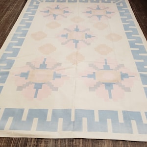 May include: A white rug with a blue and pink geometric pattern. The rug has a border of blue and white geometric shapes.