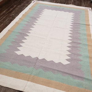 May include: A white rug with a geometric pattern in shades of beige, light green, and gray. The rug has a central white area surrounded by a border of beige, light green, and gray.