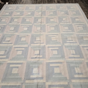 May include: A large, rectangular rug with a geometric pattern. The design features a series of squares in shades of blue, gray, and beige. The rug is made of a woven material and is suitable for a living room or bedroom.