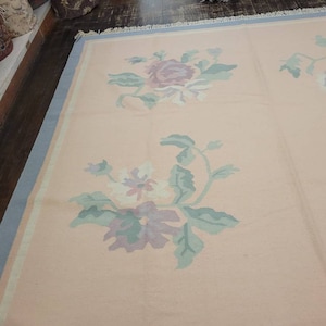 May include: A light pink rug with a blue border and a floral pattern in shades of pink, purple, and green.