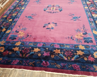 May include: A large pink rug with a floral pattern. The rug has a dark blue border with a floral design. The rug is made of wool and is in good condition.