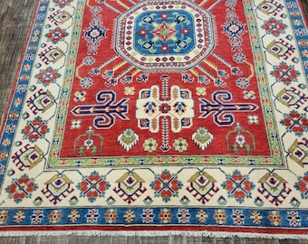 Puede incluir: Una alfombra roja, azul y crema con un diseño persa tradicional. La alfombra tiene un medallón central y un borde con intrincados patrones florales.