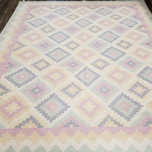 May include: A white rug with a geometric pattern in shades of pink, yellow, and gray. The rug has a diamond pattern with a border of pink and green.