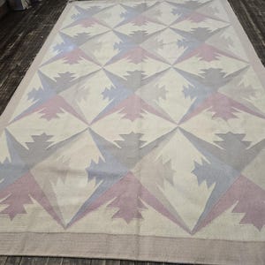 May include: A large rectangular rug with a geometric pattern. The rug features a cream-colored background with repeating starburst designs in shades of gray, lavender, and blue. The rug has a border in a matching neutral tone.