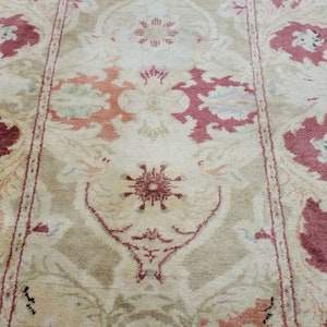 May include: A beige rug with a floral pattern in shades of pink and white. The rug has a central medallion with a starburst design and a border with repeating floral motifs.