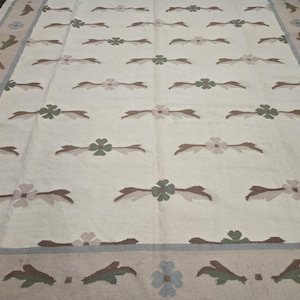 May include: Cream-colored rectangular rug with a repeating floral pattern in brown, green, and pink. The border features floral and leaf motifs in similar colors, with a light blue and tan trim.