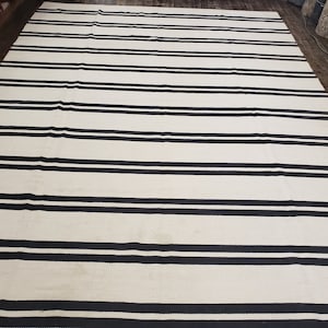 May include: A white and black striped rug with horizontal stripes. The rug is made of a woven material and has a subtle texture.