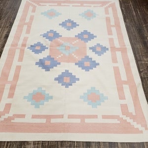 May include: A white rug with a pink border and a geometric pattern in shades of blue and light blue.