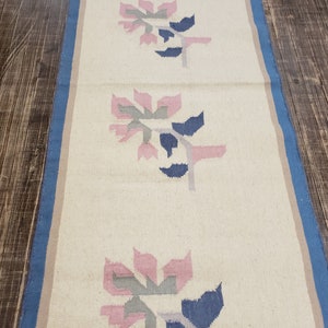 May include: A white runner rug with a blue border and a repeating pattern of pink, gray, and blue stylized flowers.
