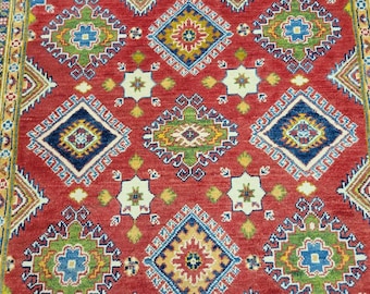 Puede incluir: Una alfombra roja con un patrón geométrico en tonos de azul, verde, amarillo y blanco. El patrón presenta formas de diamante repetidas con detalles intrincados.
