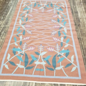 May include: A rectangular rug with a floral pattern. The rug has a light brown background with a repeating pattern of teal and light blue leaves and flowers.