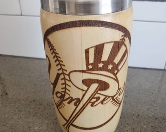 May include: A wooden baseball bat mug with a stainless steel lid. The mug is decorated with a wood-burned design of a baseball, a bat, and a hat with stars and stripes.