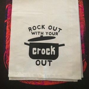 Peut inclure: Une serviette de cuisine blanche avec du texte noir qui dit "Rock out with your crock out". Le texte est dans une police stylisée et comprend une silhouette noire d'une mijoteuse.