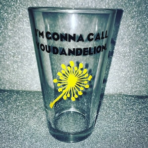 May include: A clear glass pint glass with a black and yellow design. The glass has the text "I'm gonna call you dandelion" printed on it.