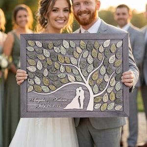 May include: A wooden wedding guest book alternative with a tree design. The grey framed sign features a tree with leaf-shaped tags for signatures. The names "Angela & Kelvin" and the date "July 26 2025" are displayed on the sign.