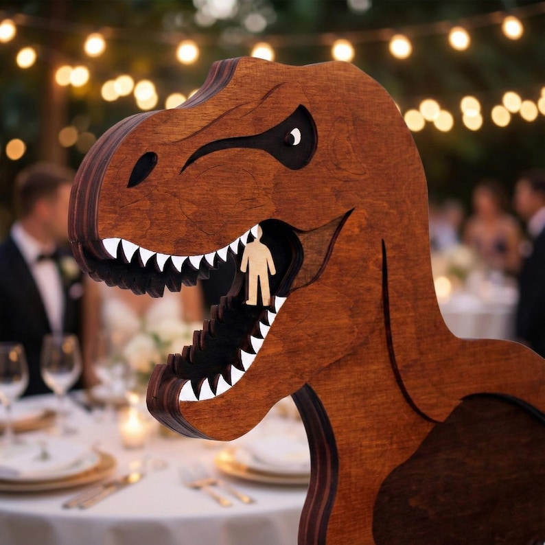 May include: A wooden Tyrannosaurus Rex sculpture with a person-shaped cutout inside its mouth. The dinosaur is brown with white teeth and a black interior. The background shows a wedding reception with string lights.