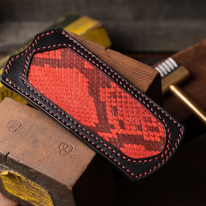 May include: A red and black leather phone case with a snakeskin pattern.
