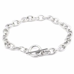 May include: A silver-colored chain bracelet with a toggle clasp. The bracelet features oval-shaped links and a circular clasp with a bar closure. The jewelry is displayed against a white background.