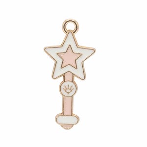 May include: Gold-tone charm with a pink and white enamel star wand design. The wand has a pink and white enamel star on top and a pink and white enamel circle with a gold eye design in the middle.