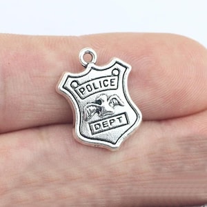 May include: Silver charm in the shape of a police badge with the words "POLICE DEPT" and a stylized bird with wings.