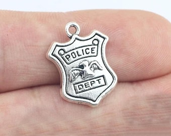May include: Silver charm in the shape of a police badge with the words "POLICE DEPT" and a stylized bird with wings.