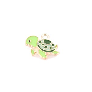 May include: A small, green and white turtle charm with a gold-colored loop for attaching to jewelry. The turtle has a green shell with dark green spots and a light green head and limbs. The charm is set against a white background.