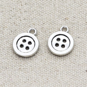 May include: Two silver-toned button charms with four holes each. The charms are round and have a loop at the top for attaching to jewelry or other crafts.