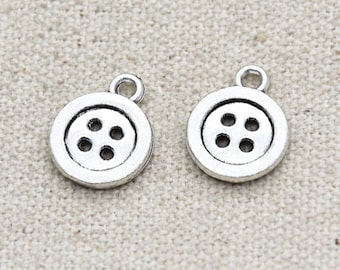 May include: Two silver-toned button charms with four holes each. The charms are round and have a loop at the top for attaching to jewelry or other crafts.