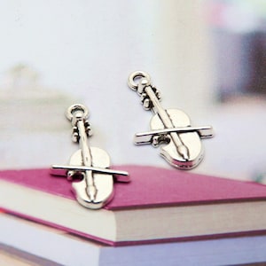 May include: Two silver-toned violin charm pendants. The charms are detailed with a violin and bow.