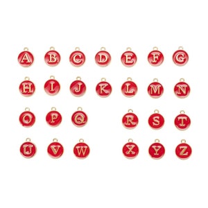 May include: Set of 26 gold-colored alphabet letter charms with red enamel. Each charm is a circle with a single letter in gold.