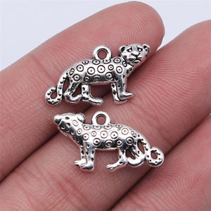 May include: Two silver-toned metal charms shaped like leopards. The charms have a spotted pattern and a loop at the top for attaching to a necklace or bracelet.