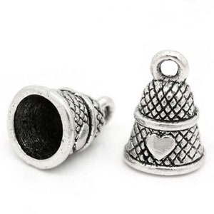 May include: Two silver-toned thimble-shaped bells with a heart design. The bells have a textured surface and a loop at the top for hanging.