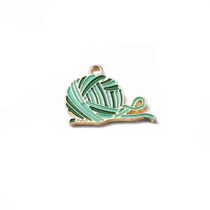 May include: A gold-colored charm in the shape of a ball of yarn. The yarn ball is green and teal with a gold outline. The charm has a loop at the top for attaching to a necklace or bracelet.