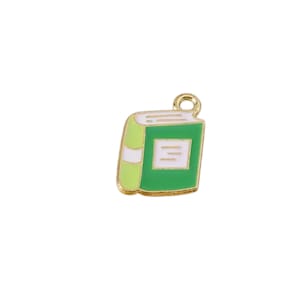 May include: A gold-colored charm in the shape of a book. The book has a green cover and spine with white and gold accents. The charm has a small loop at the top for attaching to a necklace or bracelet.