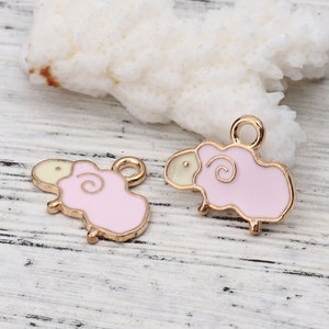 May include: Two gold-toned metal sheep charms with pink enamel bodies and cream-colored heads. The charms have a loop at the top for attaching to jewelry or other crafts. The sheep have a curly wool design.