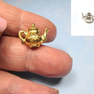 May include: A gold-colored teapot charm with a detailed design. The charm is small and has a delicate look.