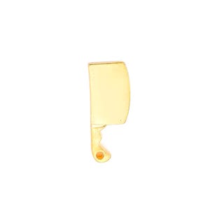 May include: A gold-colored cleaver-shaped pin. The pin has a curved blade and a handle with a small, round detail. The pin is set against a white background.