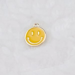 May include: A gold-colored charm with a yellow smiley face design.