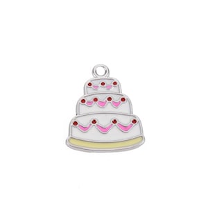 May include: A three-tiered cake charm with a white base, pink frosting accents, and red cherry details. The charm has a silver-colored loop at the top for attaching to jewelry or other crafts. The cake is outlined in a light yellow and silver.