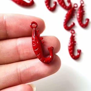 May include: Bright red shrimp-shaped charms with a loop for jewelry making. The charms have a detailed design, including the shrimp's body segments and legs. Several charms are visible against a white background.