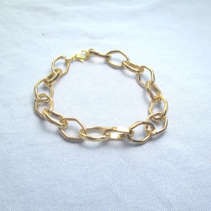 May include: A gold-colored chain bracelet with oval links. The bracelet is made of a shiny, metallic material and has a lobster clasp closure. The bracelet is displayed on a white surface.