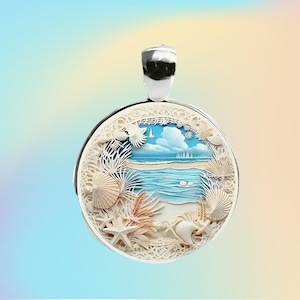 May include: A round, silver pendant with a detailed beach scene. The pendant features a layered design with seashells, starfish, and a sailboat on the ocean. The background has a blue sky with clouds. The pendant has a silver bail.