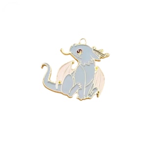 May include: A light blue dragon charm with gold-colored accents. The dragon has pink wings and red eyes. The charm is made of metal and has a loop at the top for attaching to a necklace or bracelet.