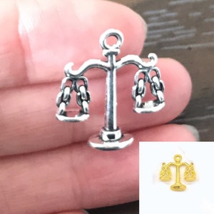 May include: Silver charm in the shape of a scale of justice. The scale is detailed with a chain design and has a small loop at the top for attaching to a necklace or bracelet.